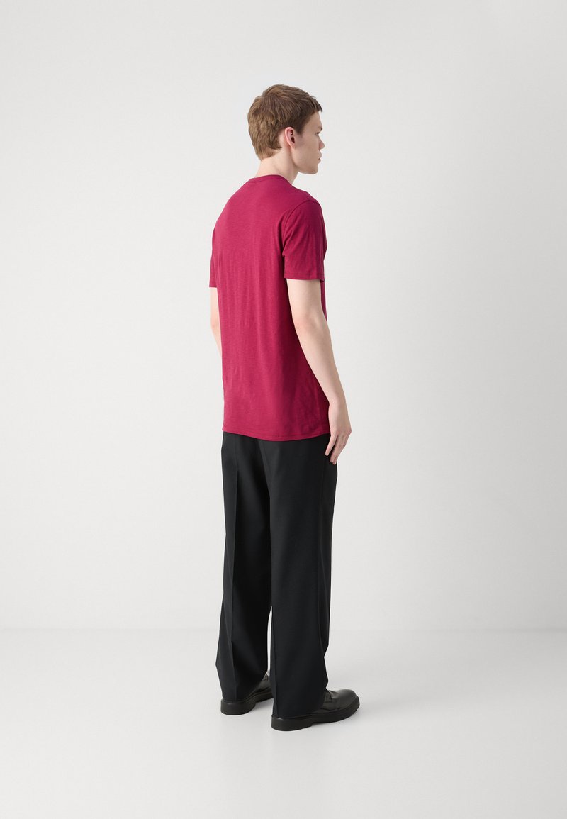 T-shirt bordeaux à manches courtes avec un col rond, associé à un pantalon noir ample et des chaussures noires, au design minimaliste.