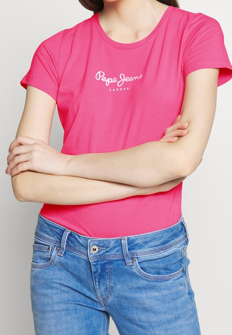 Pink cotton t-shirt with short sleeves and a round neckline, featuring a white logo text "Pepe Jeans" on the chest, paired with blue jeans.