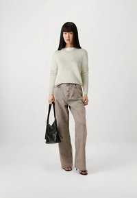 Világoszöld pulóver finom textúrával, magas derekú, bézs, bő szárú farmerrel párosítva. Fekete kézitáskával és lapos talpú szandálokkal kiegészítve.