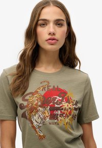 Camiseta de algodón verde oliva con un diseño de tigre texturizado y con lentejuelas en tonos rojo y dorado, cuello redondo y mangas cortas.