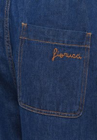 Džins tkanina stražnji džep s narančastim šavovima i "fiorucci" izvezenim narančastim koncem na džepu.