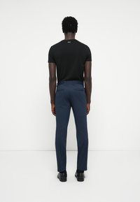 T-shirt noir à manches courtes et pantalon ajusté bleu foncé, avec une texture lisse et de subtils poches arrière, assortis de chaussures noires.
