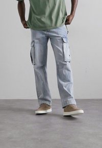 Lyseblå cargoj jeans med sidelommer, lidt løs pasform. Kombineret med en grøn t-shirt med korte ærmer og beige sneakers.