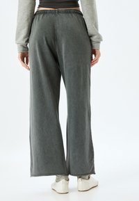 Donkergrijze wijde broek heeft een elastische tailleband met koordjes, een zachte textuur en zijsplitten aan de zoom, gecombineerd met lichte instap schoenen.