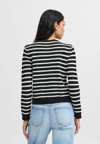 Pull à rayures noir et blanc avec un col rond, des manches longues et des poignets côtelés. Porté avec un jean bleu clair, mettant en valeur une coupe décontractée.