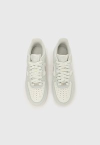 Bijele i svijetlosive Nike tenisice s perforiranim dijelom za prste, ravnim vezicama, podstavljenim ovratnikom i suptilnim brendiranjem na jeziku i bočnoj strani.