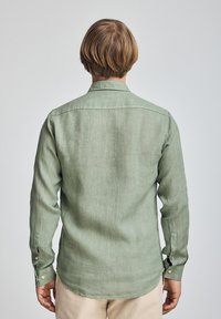 Camicia verde a maniche lunghe realizzata in un tessuto strutturato, con colletto button-down e polsini con bottoni, vista dalla schiena.