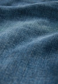 Denim material v globoko modri barvi, ki se ponaša z teksturiranim tkanjem in subtilnimi barvnimi odstopanji. Površina je gladka z rahlim sijajem.