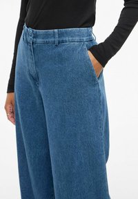 Plave traperice visokog struka s opuštenim krojem, bočnim džepovima i petljama za pojas, s mekanim, lagano teksturiranim završetkom.