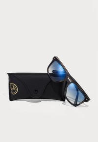 Ochelari de soare Ray-Ban negri cu lentile graduat blue, având un cadru gros și accente argintii, alături de un toc din piele neagră cu detalii logo.