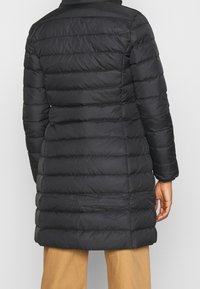 Cappotto puffo nero con design trapuntato, caratterizzato da maniche lunghe e taglio a mezza lunghezza. Texture liscia e cuciture orizzontali uniformi.