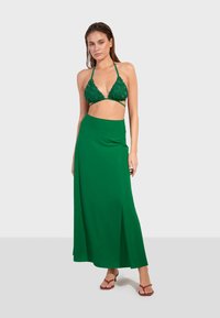 Zelený háčkovaný trojúhelníkový bikiny top v kombinácii s jednofarebnou zelenou maxi sukňou. Sukňa má vysoký pás a predný rozparok.