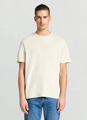 T-shirt crema a maniche corte in morbido cotone; presenta una scollatura rotonda e una vestibilità rilassata, abbinata a jeans di denim blu.