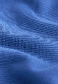 Kék szövet sima textúrával és egységes bordázott mintával, amelyen finom szín- és fényátmenetek láthatók.