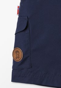 Bermudas azul-marinho feitas de um tecido resistente, com um bolso lateral e um emblema redondo de pele castanha com um design.