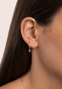 Orecchino a cerchio in oro con un pendente a forma di diamante viola. Il pendente presenta una superficie testurizzata, sospeso a un piccolo gancio.