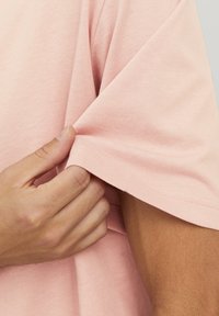 Korte mouwen roze katoenen t-shirt met een gladde textuur. De hand trekt aan de mouw om de stikseldetails te onthullen.