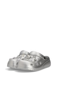 Zuecos de plata hechos de plástico suave, con acentos decorativos como perlas y adornos brillantes, con orificios para ventilación.