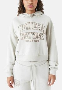 Felpa corta grigia chiara con cappuccio regolabile, caratterizzata dalla scritta "NEW ERA NEW YORK" in grassetto color crema e un tessuto testurizzato.