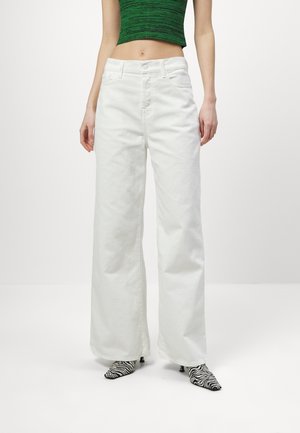 Jeans bianchi a gamba larga con vita alta, realizzati in denim. Presentano tasche frontali e chiusura con bottone. Abbinati a scarpe con stampa zebra bianca e nera.