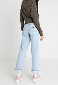 Light blue high-waisted jeans with a straight-leg cut, rolled cuffs, and embroidered patch on the back pocket, paired with a dark cropped hoodie.