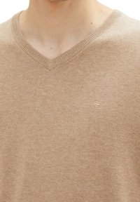 Maglione beige a scollo a V realizzato in morbido tessuto a maglia, con colletto a costine e un piccolo dettaglio del logo sul petto.