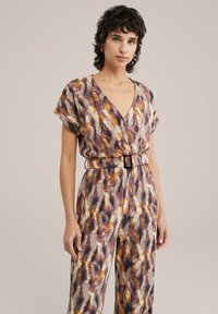 Jumpsuit a fantasia con scollatura a V profonda, maniche corte e vita cintrata. Presenta un design astratto in tonalità terrestri di arancione, marrone e crema.