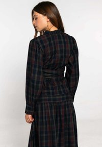 Vestido de cuadros de manga larga con un patrón de cuadros en navy oscuro y burdeos, cintura elasticada y un escote con volantes y puños abotonados.