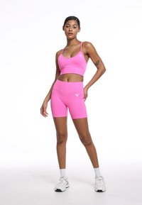 Fuksjowy stanik sportowy i dopasowane wysokie spodenki wykonane z elastycznego materiału; posiadają plecy wyścigowe i detal z logo na spodenkach.