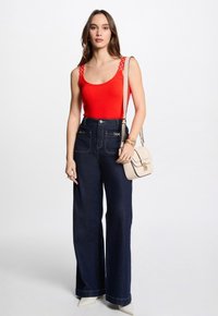 Red tank top with lace shoulder details, paired with high-waisted dark blue wide-leg jeans. Accessories include a light beige crossbody bag.