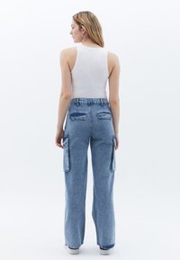 Pantalones cargo de mezclilla azul claro con cintura alta, piernas anchas y bolsillos laterales; combinados con una camiseta ajustada blanca. Vista trasera.