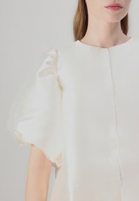 Puff-sleeved blouse in soft ivory silk with a smooth texture and subtle sheen. Features a round neckline and a straight cut.