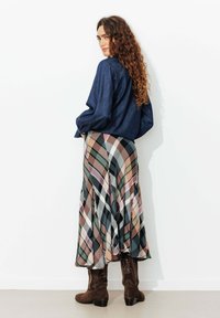 Chemise en denim associée à une jupe plissée avec un motif à carreaux multicolore dans des tons terre et des bottines en daim marron.