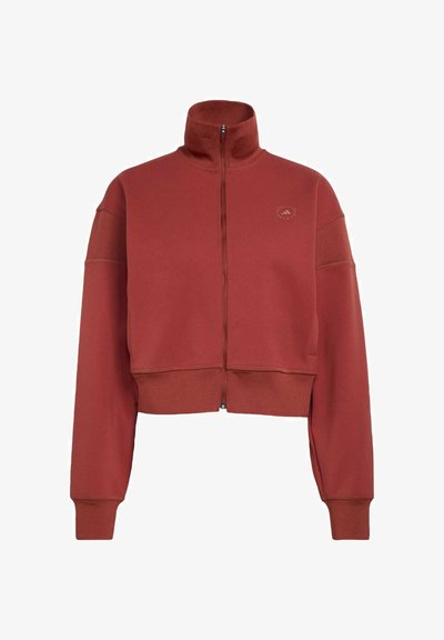 Punainen lyhyt vetoketjullinen collegetakki, jossa on korkea kaulus ja pehmeä materiaali; siinä on pitkät hihat ja hillitty logo rinnassa.