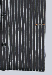 Schwarzer Stoff mit vertikalen weißen Streifen, mit Knopfverschluss und einem kleinen metallischen Logo-Akzent. Weiche Textur mit tailliertem Schnitt.