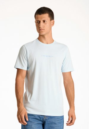 Camiseta de cuello redondo de color azul claro, hecha de algodón, con mangas cortas y un pequeño texto "LINDBERGH" en color azul claro en la zona del pecho.