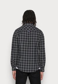 Camicia a scacchi nera e grigia con maniche lunghe, orlo arrotondato e tessuto a contrasto sul colletto. Il retro presenta un piccolo logo.