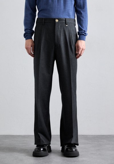Pantalons gris ajustés avec une coupe droite, une fermeture à bouton et deux plis à l'avant, associés à des chaussures à plateforme noires.
