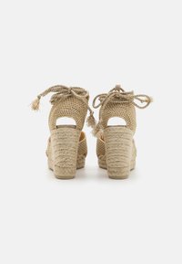 Sandales à talons hauts tissées en beige avec une finition texturée, présentant un dos fermé, des côtés ouverts et des nœuds ajustables.