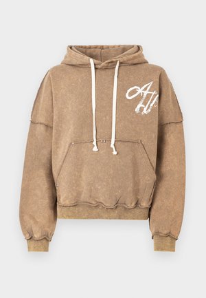 Hnedá oversize mikina s kapucňou z bavlneného materiálu, s predným vreckom a šnúrkami. Ošúchané okraje a biely logotyp na hrudi.