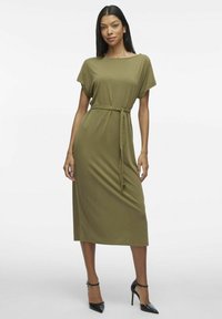 Oliwkowa midi sukienka z krótkim rękawem, luźny krój, z detalem w postaci troczków w talii. Noszona z czarnymi szpilkami. Gładka tekstura, minimalistyczny design.