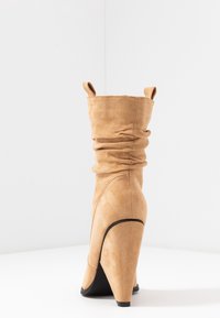 Bottes chevilles en daim fauve avec un design décontracté, talon stiletto haut, bout arrondi et petites languettes au sommet. Détail de passepoil noir.