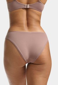 Sous-vêtements roses sans couture avec une texture lisse. Ouvertures de jambe taille haute et couverture arrière minimale, présentant une légère brillance et aucune couture visible.