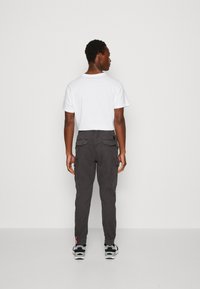 Sive cargo hlače s džepovima sa strane i straga, u kombinaciji s bijelim T-shirtom. Model nosi crno-bijele tenisice, prikazan sa stražnje strane.