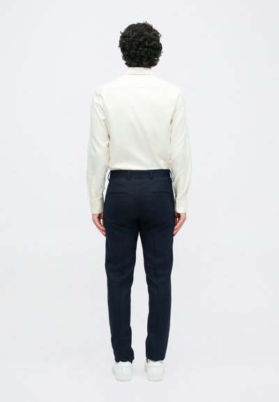 Světle krémová košile s dlouhým rukávem, námořnické kalhoty, bílé tenisky. Slim fit a hladká textura, s úpravou na míru a několika kapsami.