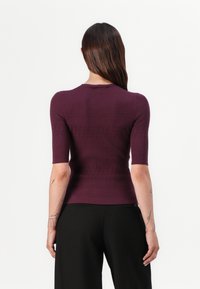 Paarse ribbel top met korte mouwen, een getailleerde silhouet en een ronde halslijn, gecombineerd met zwarte wijd-lopende broeken.