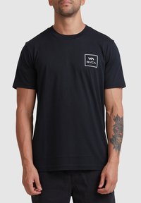 Zwart katoenen t-shirt met een wit rechthoekig logo op de linkerkant van de borst. Korte mouwen en een klassieke ronde hals.