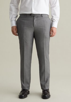 Pantalons sur mesure gris en tissu texturé, dotés d'un devant plat, de poches latérales et d'une coupe classique. Portés avec des chaussures noires.