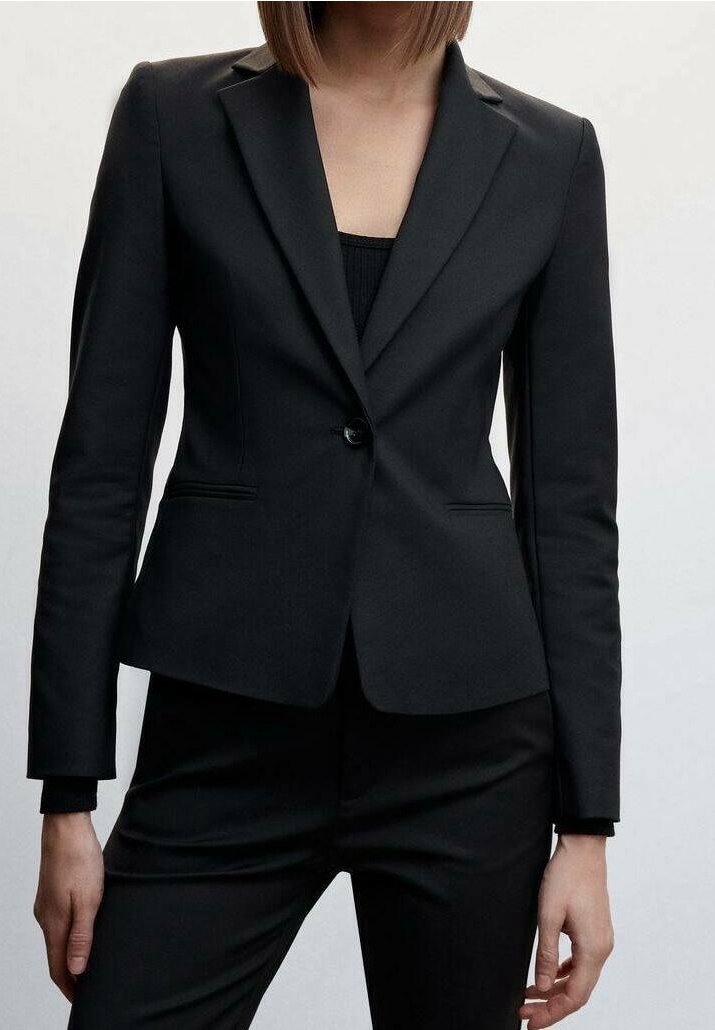 Femme portant un blazer noir ajusté avec un bouton fermé, associé à un pantalon noir et un haut noir en dessous.