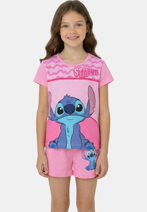 Fille portant un pyjama rose composé d'un short et d'un t-shirt avec le personnage Stitch de Disney, grand et petit, en bleu.